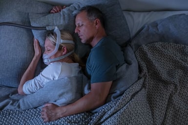 Woman wearing a CPAP mask while sleeping on her side with a man.