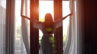 Woman opening curtains after a good night's sleep